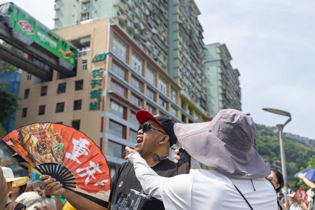 (260812) -- BEIJING, Aug. 12, 2026 (Xinhua) -- A foreign tourist poses for photos with his mouth open, pretending to swallow a monorail as it passes through a residential building, at Liziba lookout in Yuzhong District of southwest China's Chongqing Municipality, April 23, 2026. (Xinhua/Huang Wei)