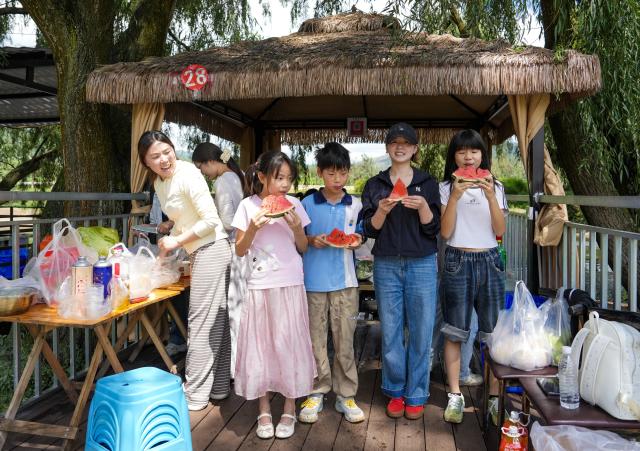 (260813) -- ZHAOTONG, Aug. 13, 2026 (Xinhua) -- Young sojourners enjoy watermelon in front of a stall in Xunlong Village of Sayu Town, Zhaoyang District in Zhaotong City, southwest China's Yunnan Province, Aug. 13, 2026. In recent years, Zhaoyang District in Zhaotong City has leveraged its cool and pleasant climate to boost the in-depth sojourn tourism experience as a summer retreat.
   The local government has introduced special support policies for summer retreat tourism, optimizing services including dining, lodging, transportation, sightseeing, shopping, and entertainment. (Xinhua/Chen Xinbo)