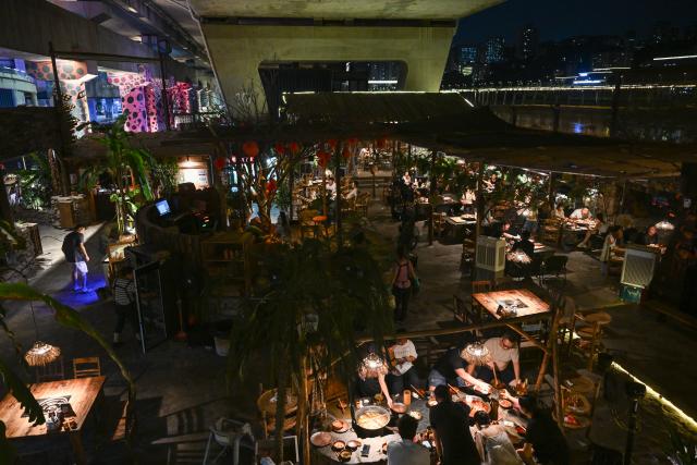 (260814) -- CHONGQING, Aug. 14, 2026 (Xinhua) -- Residents enjoy hotpots under a bridge in Liangjiang New Area, southwest China's Chongqing, Aug. 13, 2026. In recent years, Liangjiang New Area has transformed vacant spaces under bridges into spaces for exercise and recreation. (Xinhua/Chen Cheng)