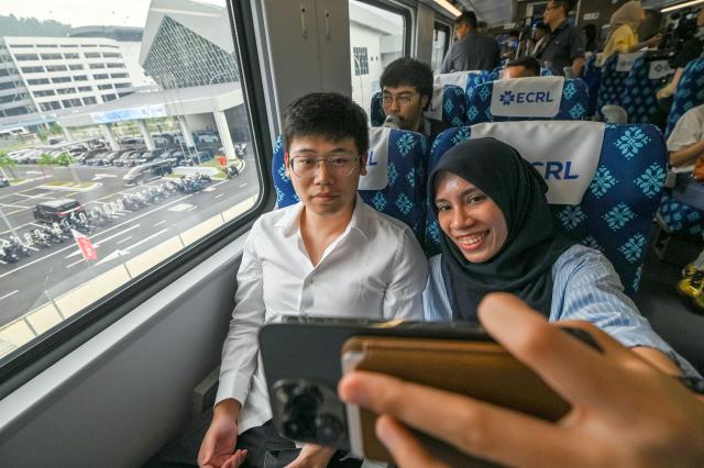 (260814) -- SELANGOR, Aug. 14, 2026 (Xinhua) -- Trial passengers take selfies aboard a train at the Gombak station of the East Coast Rail Link (ECRL) in Selangor state, Malaysia, Aug. 14, 2026. The East Coast Rail Link (ECRL), a mega rail project in Malaysia being built by the China Communications Construction Company (CCCC), is expected to begin commercial operations by January 2027, Transport Minister Anthony Loke Siew Fook said on Friday.
  In the meantime, the railway has reached 95.08 percent overall progress and has entered its testing and commissioning phase, keeping with its project schedule, Loke said in his speech at the launch ceremony of the ECRL Comprehensive Inspection Train (CIT). (Photo by Chong Voon Chung/Xinhua)