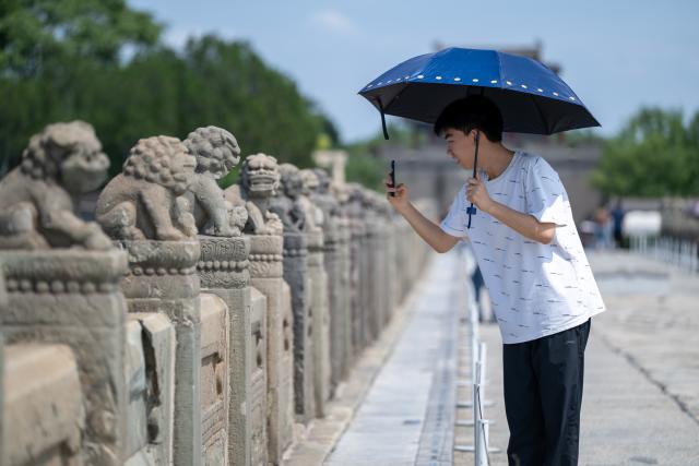 (260815) -- BEIJING, Aug. 15, 2026 (Xinhua) -- A man takes photos at the Lugou Bridge in Beijing, capital of China, Aug. 15, 2026. On July 7, 1937, Japanese soldiers attacked Chinese forces at the Lugou Bridge outside Wanping Town, marking the beginning of Japan's full-scale invasion of China, and China's whole-nation resistance against the Japanese invaders. People came to the Lugou Bridge cultural tourism area on Saturday on the occasion of the 81st anniversary of Japan's announcement of its unconditional surrender in World War II to commemorate the history. (Xinhua/Hu Jingwen)