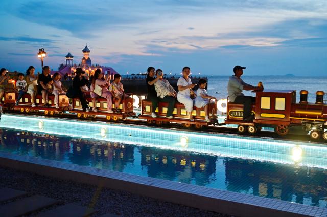 (260818) -- HUI'AN, Aug. 18, 2026 (Xinhua) -- People take a small train at the Chongwu ancient ferry terminal scenic area in Hui'an County of Quanzhou, southeast China's Fujian Province, Aug. 17, 2026. The Chongwu ancient ferry terminal covers an area of 33 mu (about 2.2 hectares) in Hui'an County of southeast China's Fujian Province. In 2024, local authorities transformed it from an idle terminal into a coastal vacation destination that integrates art galleries, a pier runway, trendy restaurants, and family playgrounds. (Xinhua/Lin Shanchuan)