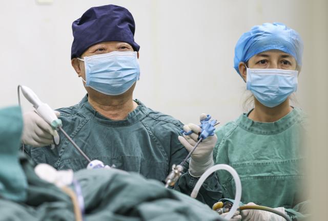 (260819) -- URUMQI, Aug. 19, 2026 (Xinhua) -- Zhuang Shihua (L) performs a surgery at the hospital affiliated to the Xinjiang Armed Police Corps in Urumqi, northwest China's Xinjiang Uygur Autonomous Region, Aug. 18, 2026.
  Zhuang Shihua, a veteran hepatobiliary surgeon and former president of the hospital affiliated to the Xinjiang Armed Police Corps, has been in the country's far west for over five decades.
  His team has successfully completed more than 140,000 minimally invasive hepatobiliary surgeries, and made seven breakthroughs that filled the domestic gap in the field. Apart from clinical practice, Zhuang has cultivated a large number of key personnel, and supported grassroots medical workers who have stood firm on the front lines of public health.
  Zhuang's medical expertise brought him many opportunities to make a fortune, but he turned down the offers and stayed in Xinjiang.
  Zhuang often visited patients in the pastoral areas of Tianshan Mountains. He also provided financial assistance to over 70 underprivileged students and helped more than 690 households with patients out of poverty. (Xinhua/Wang Fei)