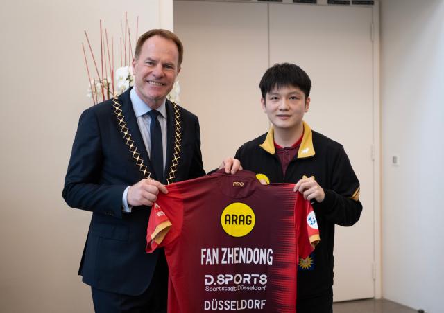 (260821) -- BEIJING, Aug. 21, 2026 (Xinhua) -- Fan Zhendong (R) gives his jersey to Stephan Keller, mayor of Dusseldorf, during the welcoming ceremony in Dusseldorf, Germany, Aug. 20, 2026. Chinese table tennis star Fan Zhendong was officially unveiled by his new club Borussia Dusseldorf at a press conference here on Thursday, as the Olympic champion prepares for his second season in the German Table Tennis Bundesliga and another campaign in European competition. (Xinhua/Zhang Haofu)