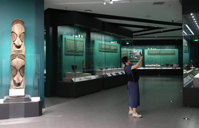 (260821) -- PINGTAN, Aug. 21, 2026 (Xinhua) -- A woman takes photos during the exhibition "Austronesian Art: The Bowers Museum's Collection" at the Keqiutou Site Museum in Pingtan, southeast China's Fujian Province, Aug. 20, 2026. Keqiutou Site Museum, a branch of the Chinese Archaeological Museum, is built around the Keqiutou ruins. It serves as an important platform for the study and presentation of Austronesian culture and for the display of the prehistoric culture of Pingtan. (Xinhua/Du Xiaoyi)