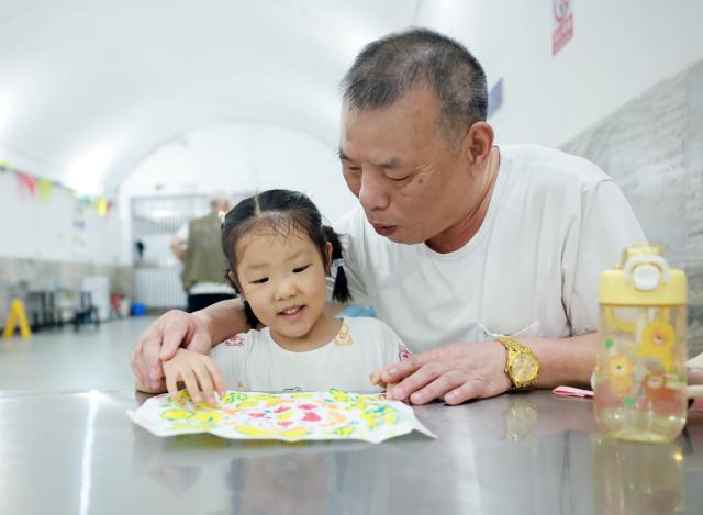 (260821) -- WUHAN, Aug. 21, 2026 (Xinhua) -- A girl looks at a painting with her guardian at a civil-defense facility which has been opened as a public cooling space in Wuhan, central China's Hubei Province, July 14, 2026. (Photo by Zhao Jun/Xinhua)