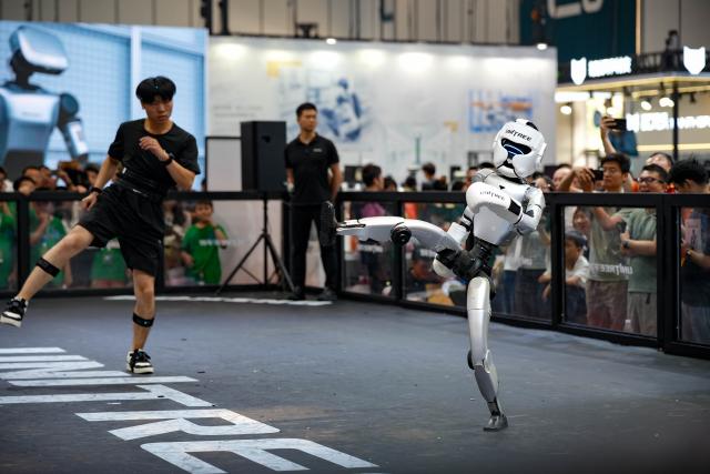 (260821) -- BEIJING, Aug. 21, 2026 (Xinhua) -- A robot and a staff member demonstrate human-robot collaboration during the 2026 World Robot Conference in Beijing, capital of China, Aug. 20, 2026. The conference, which runs from Wednesday through Sunday, has drawn more than 300 exhibitors from 26 countries, with over 3,000 products on display, including more than 300 debuts. (Xinhua/Xie Han)