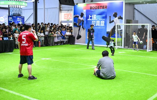 (260822) -- BEIJING, Aug. 22, 2026 (Xinhua) -- A robot takes a penalty kick as a boy plays as the goalkeeper at the 2026 World Robot Conference in Beijing, capital of China, Aug. 22, 2026. The conference, which runs from Wednesday through Sunday, has drawn more than 300 exhibitors from 26 countries, with over 3,000 products on display, including more than 300 debuts. Many people visited the conference on Saturday, the first open day of the event. (Xinhua/Chen Yehua)