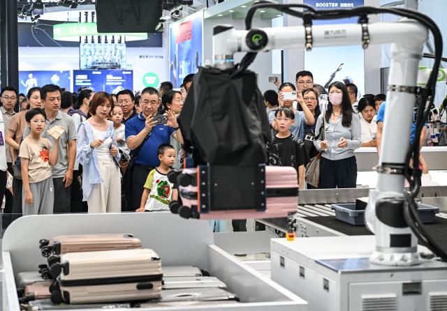 (260822) -- BEIJING, Aug. 22, 2026 (Xinhua) -- People view a robotic arm carrying a suitcase through a security screening machine at the 2026 World Robot Conference in Beijing, capital of China, Aug. 22, 2026. The conference, which runs from Wednesday through Sunday, has drawn more than 300 exhibitors from 26 countries, with over 3,000 products on display, including more than 300 debuts. Many people visited the conference on Saturday, the first open day of the event. (Xinhua/Chen Yehua)