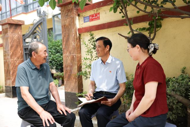 (260822) -- LIANYUNGANG, Aug. 22, 2026 (Xinhua) -- Zhong Baijun (C) visits a senior villager in Xijidang Village, Zhewang Town of Lianyungang City, east China's Jiangsu Province, June 25, 2026. Zhong Baijun, Party secretary of Xijidang Village and head of the village committee, has spent 28 years serving his hometown in Zhewang Town of Lianyungang City, east China's Jiangsu Province.
  When he returned to the village to take up his post in 1998, the village collective had no industries and was in debt. Most residents made a living from farming, and many younger villagers left home to seek work elsewhere.
  Looking for new ways to develop the local economy, Zhong and other village officials traveled to other areas to explore potential industries. Leveraging the village's coastal location and the relatively abundant stock of discarded fishing nets, they gradually developed a nylon pellet processing industry.
  The industry initially grew through small workshops. To restructure the sector, the village invested 120 million yuan (about 17.9 million U.S. dollars) in building a standardized industrial park and later developed a model that allowed residents to benefit from the industry's growth through shareholding, local employment and dividends. By 2025, Xijidang's total industrial output reached 2.5 billion yuan (about 372 million U.S. dollars). The industry also created jobs for more than 1,600 local residents.
  As the collective economy grew, the village put more resources into improving community well-being. It organized cultural and sports activities, as well as model-family award campaigns, giving residents more opportunities to take part in community events.
  Over the past 28 years, Zhong has witnessed the village's industries expand, employment opportunities increase and collective income rise. "We should put the people's concerns first," Zhong said. (Photo by Si Wei/Xinhua)