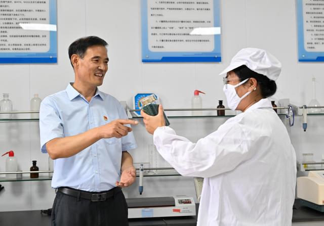 (260822) -- LIANYUNGANG, Aug. 22, 2026 (Xinhua) -- Zhong Baijun (L) learns about the research and development of products at a laboratory in a circular economy industrial park in Xijidang Village, Zhewang Town of Lianyungang City, east China's Jiangsu Province, Aug. 19, 2026. Zhong Baijun, Party secretary of Xijidang Village and head of the village committee, has spent 28 years serving his hometown in Zhewang Town of Lianyungang City, east China's Jiangsu Province.
  When he returned to the village to take up his post in 1998, the village collective had no industries and was in debt. Most residents made a living from farming, and many younger villagers left home to seek work elsewhere.
  Looking for new ways to develop the local economy, Zhong and other village officials traveled to other areas to explore potential industries. Leveraging the village's coastal location and the relatively abundant stock of discarded fishing nets, they gradually developed a nylon pellet processing industry.
  The industry initially grew through small workshops. To restructure the sector, the village invested 120 million yuan (about 17.9 million U.S. dollars) in building a standardized industrial park and later developed a model that allowed residents to benefit from the industry's growth through shareholding, local employment and dividends. By 2025, Xijidang's total industrial output reached 2.5 billion yuan (about 372 million U.S. dollars). The industry also created jobs for more than 1,600 local residents.
  As the collective economy grew, the village put more resources into improving community well-being. It organized cultural and sports activities, as well as model-family award campaigns, giving residents more opportunities to take part in community events.
  Over the past 28 years, Zhong has witnessed the village's industries expand, employment opportunities increase and collective income rise. "We should put the people's concerns first," Zhong said. (Xinhua/Ji Chunpeng)