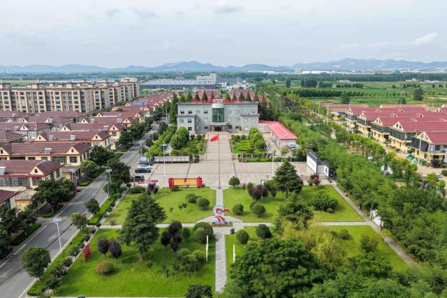 (260822) -- LIANYUNGANG, Aug. 22, 2026 (Xinhua) -- An aerial drone photo taken on Aug. 19, 2026 shows a view of the Xijidang Village, Zhewang Town of Lianyungang City, east China's Jiangsu Province. Zhong Baijun, Party secretary of Xijidang Village and head of the village committee, has spent 28 years serving his hometown in Zhewang Town of Lianyungang City, east China's Jiangsu Province.
  When he returned to the village to take up his post in 1998, the village collective had no industries and was in debt. Most residents made a living from farming, and many younger villagers left home to seek work elsewhere.
  Looking for new ways to develop the local economy, Zhong and other village officials traveled to other areas to explore potential industries. Leveraging the village's coastal location and the relatively abundant stock of discarded fishing nets, they gradually developed a nylon pellet processing industry.
  The industry initially grew through small workshops. To restructure the sector, the village invested 120 million yuan (about 17.9 million U.S. dollars) in building a standardized industrial park and later developed a model that allowed residents to benefit from the industry's growth through shareholding, local employment and dividends. By 2025, Xijidang's total industrial output reached 2.5 billion yuan (about 372 million U.S. dollars). The industry also created jobs for more than 1,600 local residents.
  As the collective economy grew, the village put more resources into improving community well-being. It organized cultural and sports activities, as well as model-family award campaigns, giving residents more opportunities to take part in community events.
  Over the past 28 years, Zhong has witnessed the village's industries expand, employment opportunities increase and collective income rise. "We should put the people's concerns first," Zhong said. (Photo by Si Wei/Xinhua)
