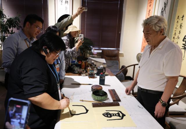 (260822) -- DALIAN, Aug. 22, 2026 (Xinhua) -- Delegates attending the Third APEC Senior Officials' Meeting and Related Meetings experience calligraphy at a historical and cultural neighborhood in Dalian, northeast China's Liaoning Province, Aug. 22, 2026. The Third APEC Senior Officials' Meeting and Related Meetings are held here from Aug. 17 to 28. (Xinhua/Li Gang)