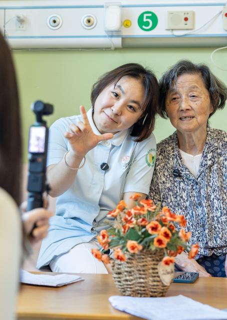 (260823) -- HUZHOU, Aug. 23, 2026 (Xinhua) -- Shen Wanting (L) and a senior resident are filmed during a video shoot in Huzhou City, east China's Zhejiang Province, Aug. 17, 2026.
  Senior residents at the Shushan Healthcare Center, an elderly care center in Huzhou, Zhejiang Province, sometimes misunderstand one another during daily conversations because of their advanced age. These moments inspired Shen Wanting, a post-95 nurse, and five colleagues of similar age to create micro dramas featuring these elderly residents and their daily lives at the center. 
  Five senior residents, whose average age is over 80, are regular cast members, and the oldest is over 90. 
  After gaining attention online, the production team has continued to release micro drama episodes. Since June 2025, they have produced over 160 episodes. (Photo by Yi Fan/Xinhua)