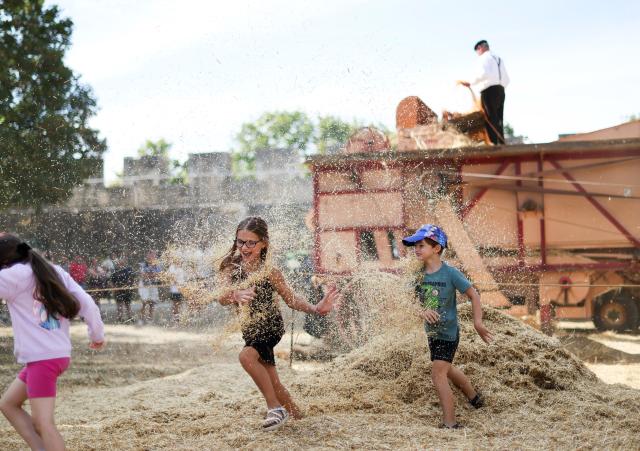 (260824) -- BEIJING, Aug. 24, 2026 (Xinhua) -- Children play near a traditional threshing demonstration during the Harvest Festival in Provins, France, Aug. 23, 2026. The medieval town of Provins celebrated its Harvest Festival on Sunday, featuring float parades, traditional threshing demonstrations, vintage tractors and folk dances. (Xinhua/Wu Huiwo)