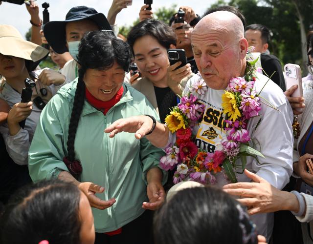 (260824) -- ORDOS, Aug. 24, 2026 (Xinhua) -- Ronald Sakolsky interacts with Yin Yuzhen's grandchildren after he arrives at her home in Salawusu Village, Uxin Banner, north China's Inner Mongolia Autonomous Region, Aug. 24, 2026. Retired U.S. teacher Ronald Sakolsky, who once supported China's desertification control efforts, arrived in Ordos on Sunday and was reunited with his friend Yin Yuzhen, a national model worker who has been planting trees in the Maowusu Sandy Land for four decades. He then visited her home on Monday.
   Their story began in 1999, when Sakolsky taught English at a school in central China's Henan Province under a teachers' exchange program between the two countries.
   After watching a television news report featuring Yin's tireless work, he was deeply moved and raised 5,000 U.S. dollars to help Yin and her husband in their afforestation efforts against desertification.
   The saplings bought and planted with that donation have since grown into a forest of more than 50,000 towering trees. (Xinhua/Lian Zhen)