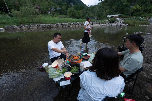 (260824) -- GUANGYUAN, Aug. 24, 2026 (Xinhua) -- Tourists picnic in the shallows of a stream in Zengjiashan scenic spot of Guangyuan City, southwest China's Sichuan Province, Aug. 23, 2026. Zengjiashan, a summer getaway with an average elevation of 1,300 meters and summer temperatures of around 23 degrees centigrade, is developing tourism by making the most of its cool climate, attracting visitors from surrounding areas. (Xinhua/Jiang Hongjing)