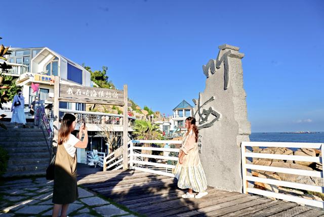 (260824) -- FUZHOU, Aug. 24, 2026 (Xinhua) -- Tourists take photos at a scenic spot in Dazuo Village of Hui'an County, southeast China's Fujian Province, Aug. 17, 2026. Dazuo Village is surrounded by the sea on three sides. In recent years, the village has focused on cultivating the traditional customs, launching experiential activities such as net weaving and travel photography to attract tourists. (Xinhua/Lin Shanchuan)
