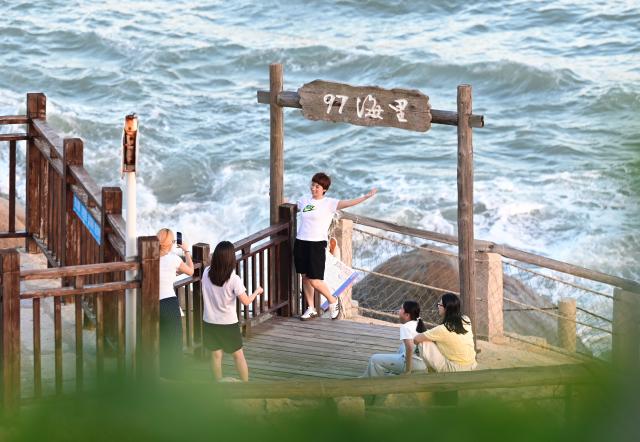 (260824) -- FUZHOU, Aug. 24, 2026 (Xinhua) -- Tourists take photos at a scenic spot in Dazuo Village of Hui'an County, southeast China's Fujian Province, Aug. 17, 2026. Dazuo Village is surrounded by the sea on three sides. In recent years, the village has focused on cultivating the traditional customs, launching experiential activities such as net weaving and travel photography to attract tourists. (Xinhua/Lin Shanchuan)
