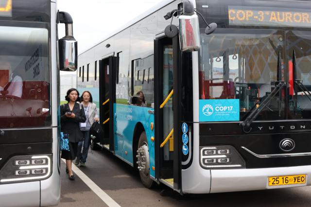 (260825) -- ULAN BATOR, Aug. 25, 2026 (Xinhua) -- Guests attending the 17th session of the Conference of the Parties (COP17) to the United Nations Convention to Combat Desertification (UNCCD) are seen beside buses produced by Chinese electric bus manufacturer Yutong Bus Co., Ltd., a transportation partner authorized for the event, in Ulan Bator, Mongolia, Aug. 17, 2026. (Xinhua/Bolortsetseg)