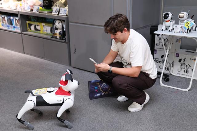 (260827) -- BEIJING, Aug. 27, 2026 (Xinhua) -- A member of a joint China-Russia media delegation interacts with a robot dog at a robot 6S store in Longgang District of Shenzhen, south China's Guangdong Province, Aug. 26, 2026.
  The delegation visited Hangzhou, Wuhan and Shenzhen in recent days to learn about the AI robotics industry. (Xinhua/Liang Xu)