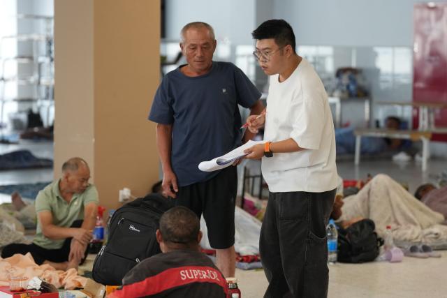 (260827) -- HANGZHOU, Aug. 27, 2026 (Xinhua) -- A staff member (R) inquires about people's need at a resettlement site at a middle school in Yuhuan City, east China's Zhejiang Province, Aug. 27, 2026. East China's Zhejiang Province raised its typhoon emergency response to Level I, the highest level, at 8 p.m. Thursday as Typhoon Saudel, the 18th typhoon of this year, is forecast to make landfall in the province. (Xinhua/Huang Zongzhi)