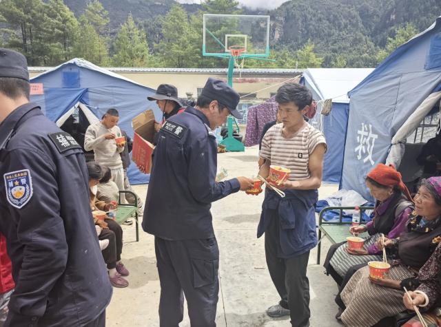 (260827) -- GYIRONG, Aug. 27, 2026 (Xinhua) -- Auxiliary police officers distribute food at a temporary shelter in Gyirong County in Xigaze, southwest China's Xizang Autonomous Region, Aug. 27, 2026. The first batch of 26 rescue officers from the local public security authorities in Gyirong have set up 24 emergency tents in the courtyard of a township government compound and evacuated more than 320 residents affected by a mudslide in Gyirong County. (Xinhua)