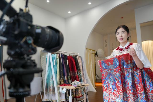 (260828) -- HEZE, Aug. 28, 2026 (Xinhua) -- A staff member promotes hanfu via livestreaming in Caoxian County of Heze City, east China's Shandong Province, Aug. 27, 2026.
  Caoxian County, a major production hub for original hanfu designs, recorded 13 billion yuan (about 1.9 billion U.S. dollars) in hanfu sales in 2025.
  With a complete industrial chain in place, the county is expanding into doll clothing, ethnic apparel and humanoid robots costumes, showcasing the continued upgrading of its clothing industry. (Xinhua/Dai Mingxuan)