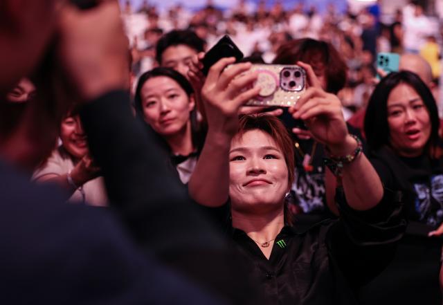 (260829) -- SHANGHAI, Aug. 29, 2026 (Xinhua) -- Zhang Weili, China's first-ever UFC (Ultimate Fighting Championship) world champion, takes pictures with her phone during the UFC Fight Night Flyweight Bout 3 Rounds at the Oriental Sports Center in east China's Shanghai, Aug. 29, 2026. (Xinhua/Li Ming)
