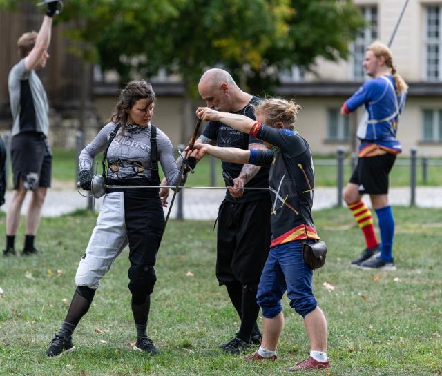 (260831) -- POTSDAM, Aug. 31, 2026 (Xinhua) -- A trainer (C) talks with enthusiasts as they practice swordsmanship at Sanssouci Park in Potsdam, Germany, Aug. 30, 2026.
  Swordsmanship enthusiasts gathered here on Sunday to practice and exchange skills in historical European swordsmanship against the backdrop of the city's iconic historic architecture. (Xinhua/Zhang Haofu)