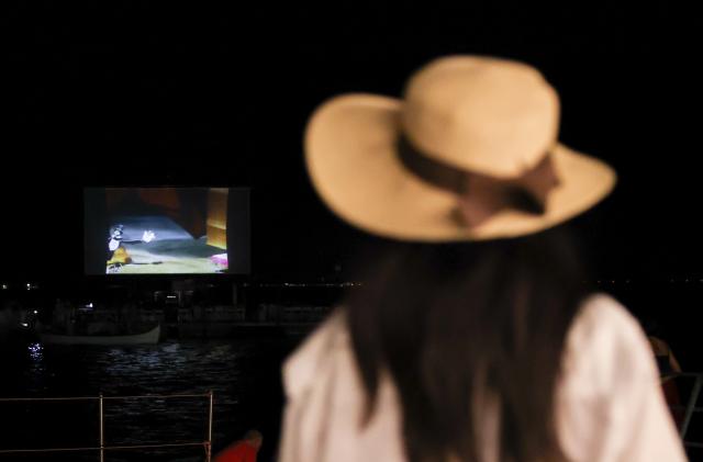 (260904) -- VENICE, Sept. 4, 2026 (Xinhua) -- A woman watches a movie at the "Floating Cinema - Unknown Waters" event in Venice, Italy, Sept. 4, 2026. "Floating Cinema - Unknown Waters" offers a cultural event in the waters behind the island of Giudecca in the Venice Lagoon. The festival features a floating stage, viewable from private boats or a shared floating platform, where attendees can enjoy a diverse array of screenings and performances by both international and local artists. (Xinhua/Wang Kaiyan)
