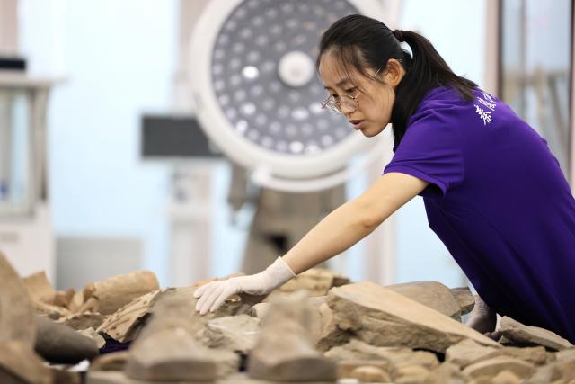 (260909) -- XI'AN, Sept. 9, 2026 (Xinhua) -- A restoration specialist checks excavated terracotta warrior fragments at the on-site conservation lab of the Pit No.1 of the Emperor Qinshihuang's Mausoleum Site Museum in Xi'an, northwest China's Shaanxi Province, Sept. 3, 2026.
  At the world-famous Terracotta Warriors site in Xi'an, visitors can now witness a once behind-the-scenes process -- experts meticulously restoring over 2,000-year-old clay soldiers. At the newly launched conservation lab in Pit No. 1, specialists piece fragmented pottery together manually, reviving scattered relics into solemn and life-size warriors.
  The lab officially opened in 2024, celebrating the 50th anniversary of the discovery and excavation of the iconic Terracotta Warriors. A professional excavation and preservation facility in Pit No. 2 was also completed and put into operation. The two facilities form a full-cycle conservation system covering excavation, transportation, restoration and storage. 
  This advanced system greatly improves the protection of the warriors' original pigments. Buried underground for over 2,000 years, the Terracotta Warriors suffered severe damage from fires, soil collapses and underground water fluctuations, with most original colors fading away over time. Previously, surviving paint layer would easily curl, peel or flake off once exposed to drastic environmental changes after excavation. Today, newly unearthed painted relics are directly transferred to the on-site lab. Through keeping stable humidity control, ultrasonic inspection, 3D scanning, professional cleaning and reinforcement treatment, researchers now do their utmost to preserve the warriors' ancient original hues. (Xinhua/Li Yibo)