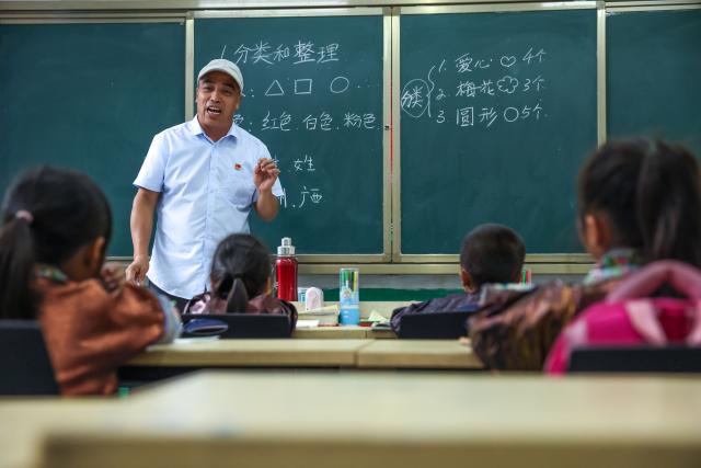(260913) -- CONGJIANG, Sept. 13, 2026 (Xinhua) -- Pan Xianfeng teaches students at the Wuying teaching site in Wuying Village on the border between south China's Guangxi Zhuang Autonomous Region and southwest China's Guizhou Province, Sept. 2, 2026. Deep in the mountains on the border between south China's Guangxi Zhuang Autonomous Region and southwest China's Guizhou Province, Wuying Village is far from the township central school. To solve the problem of children having to travel long distances to school, the Wuying teaching site has been retained to this day. This semester it has only two teachers, 56-year-old Pan Xianfeng from Guizhou and 29-year-old Peng Hanping from Guangxi, and 10 students, making it a "micro-primary school." 
   Due to its remote location and harsh conditions, few teachers are willing to teach here for long. Pan applied to transfer here in March 2020 from a better-equipped rural school in Guizhou and Peng followed in September 2023 from a Guangxi primary school. The two, from different provinces and belong to different generations, work in close coordination to keep the school running. 
   Beyond the classroom, they have volunteered at the village night school, teaching local residents literacy and Mandarin, broadening their perspectives and paving way for better livelihoods. 
   "Even with only one student, the teaching site must continue," Pan said firmly. Peng added, "It is all worthwhile so long as the children can go to school nearby, no matter how difficult the work gets." (Xinhua/Yang Wenbin)