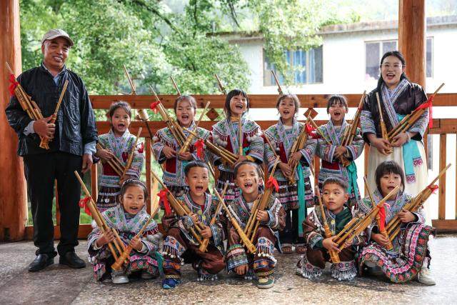 (260913) -- CONGJIANG, Sept. 13, 2026 (Xinhua) -- Pan Xianfeng (1st L) and Peng Hanping (1st R) pose for a group photo with students at the Wuying teaching site in Wuying Village on the border between south China's Guangxi Zhuang Autonomous Region and southwest China's Guizhou Province, Sept. 4, 2026. Deep in the mountains on the border between south China's Guangxi Zhuang Autonomous Region and southwest China's Guizhou Province, Wuying Village is far from the township central school. To solve the problem of children having to travel long distances to school, the Wuying teaching site has been retained to this day. This semester it has only two teachers, 56-year-old Pan Xianfeng from Guizhou and 29-year-old Peng Hanping from Guangxi, and 10 students, making it a "micro-primary school." 
   Due to its remote location and harsh conditions, few teachers are willing to teach here for long. Pan applied to transfer here in March 2020 from a better-equipped rural school in Guizhou and Peng followed in September 2023 from a Guangxi primary school. The two, from different provinces and belong to different generations, work in close coordination to keep the school running. 
   Beyond the classroom, they have volunteered at the village night school, teaching local residents literacy and Mandarin, broadening their perspectives and paving way for better livelihoods. 
   "Even with only one student, the teaching site must continue," Pan said firmly. Peng added, "It is all worthwhile so long as the children can go to school nearby, no matter how difficult the work gets." (Xinhua/Yang Wenbin)