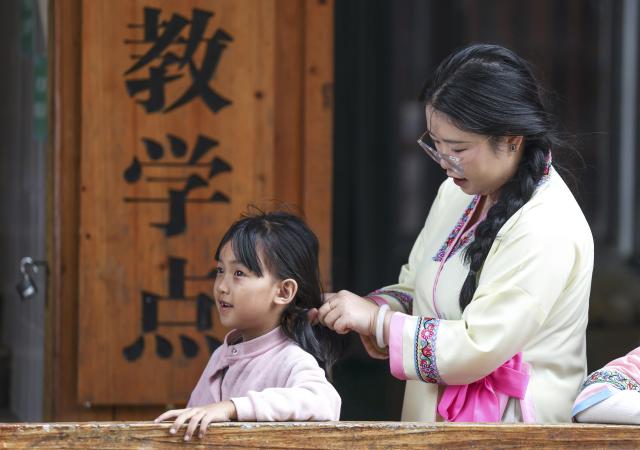 (260913) -- CONGJIANG, Sept. 13, 2026 (Xinhua) -- Peng Hanping helps a student tie her hair at the Wuying teaching site in Wuying Village on the border between south China's Guangxi Zhuang Autonomous Region and southwest China's Guizhou Province, Sept. 3, 2026. Deep in the mountains on the border between south China's Guangxi Zhuang Autonomous Region and southwest China's Guizhou Province, Wuying Village is far from the township central school. To solve the problem of children having to travel long distances to school, the Wuying teaching site has been retained to this day. This semester it has only two teachers, 56-year-old Pan Xianfeng from Guizhou and 29-year-old Peng Hanping from Guangxi, and 10 students, making it a "micro-primary school." 
   Due to its remote location and harsh conditions, few teachers are willing to teach here for long. Pan applied to transfer here in March 2020 from a better-equipped rural school in Guizhou and Peng followed in September 2023 from a Guangxi primary school. The two, from different provinces and belong to different generations, work in close coordination to keep the school running. 
   Beyond the classroom, they have volunteered at the village night school, teaching local residents literacy and Mandarin, broadening their perspectives and paving way for better livelihoods. 
   "Even with only one student, the teaching site must continue," Pan said firmly. Peng added, "It is all worthwhile so long as the children can go to school nearby, no matter how difficult the work gets." (Xinhua/Yang Wenbin)