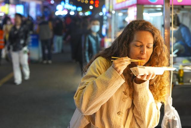 (260916) -- BEIJING, Sept. 16, 2026 (Xinhua) -- A Russian tourist tastes food at a night market in Heihe, northeast China's Heilongjiang Province, Sept. 15, 2026. Cross-border tourism and people-to-people exchanges between China and Russia have become more active since the introduction of optimized visa-free policies in 2025. (Xinhua/Na Yuqi)