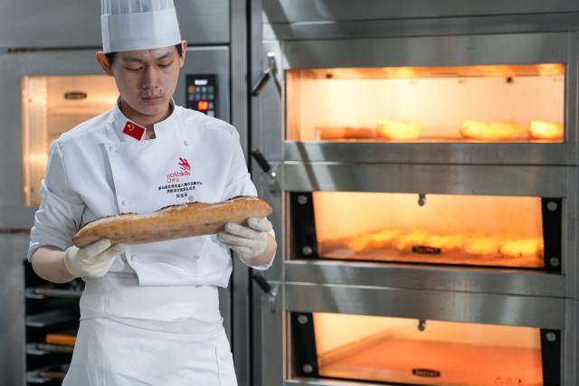 (260919) -- SUZHOU, Sept. 19, 2026 (Xinhua) -- Hou Jinchen checks the condition of baguette at Suzhou Wuzhong Technician College in Suzhou, east China's Jiangsu Province, Aug. 27, 2026. Born in 2005, Hou Jinchen studies culinary arts at Suzhou Wuzhong Technician College. He began learning to bake at the age of 12, and his passion for it has grown ever since.
   From shaping dough to baking and decorating bread, Hou follows a rigorous training routine. He practices the same techniques over and over to build muscle memory, carefully recording changes in temperature and ingredient quantities during each session and constantly refining the details.
   Outside training, he also visits local bakeries to learn from working bakers. He believes they have a better understanding of consumer preferences, which gives him insights that training focused solely on competitions may not always provide.
   His efforts have earned him both gold and bronze medals in national vocational skills competitions, and he was later selected for the national team. The 21-year-old is now preparing for the upcoming WorldSkills Competition in Shanghai.
   Among all the competition tasks, Hou devotes particular attention to artistic bread design. From sketching ideas to making molds and baking the final pieces, the process requires repeated adjustments. He sometimes uses 3D-printed molds and plans to incorporate more Chinese elements into his competition pieces in Shanghai.
   For Hou, baking is not just a technical skill, but also a pursuit of craftsmanship. He hopes to showcase the skills and dedication of young Chinese bakers on the international stage.
   "I can't imagine leaving the baking industry," Hou said. "In the future, I hope to become a coach and pass on what I have learned to younger bakers." (Xinhua/Li Bo)