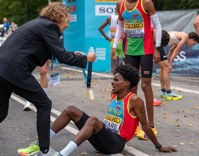 (260920) -- COPENHAGEN, Sept. 20, 2026 (Xinhua) -- Dawit Seare (bottom) of Eritrea receives his gold medal while seating on the ground after the men's 5km race at the World Athletics Road Running Championships in Copenhagen, Denmark, Sept. 19, 2026. (Photo by Anders Kongshaug/Xinhua)