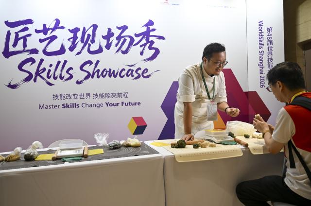 (260921) -- SHANGHAI, Sept. 21, 2026 (Xinhua) -- A media staff member (R) tries making mooncakes at the media center of the 48th WorldSkills Competition in Shanghai, east China, Sept. 21, 2026. The 48th WorldSkills Competition is scheduled to take place from September 22 to 27 in Shanghai. (Xinhua/Chen Haoming)