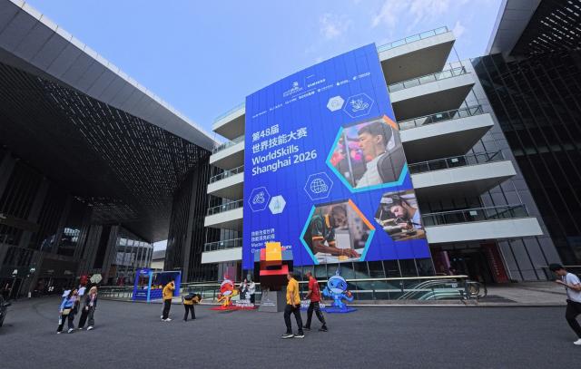 (260921) -- SHANGHAI, Sept. 21, 2026 (Xinhua) -- People walk past the decorations for the 48th WorldSkills Competition at the National Exhibition and Convention Center (Shanghai) in east China's Shanghai, Sept. 21, 2026. The 48th WorldSkills Competition is scheduled to take place from September 22 to 27 in Shanghai. (Xinhua/Fang Zhe)