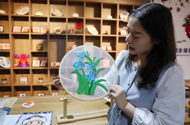 (260921) -- GUYUAN, Sept. 21, 2026 (Xinhua) -- A staff member introduces a Duoxiu embroidery work at a study tour base in Yuanzhou District, Guyuan City of northwest China's Ningxia Hui Autonomous Region, Sept. 21, 2026. Yuanzhou District in Guyuan City has developed an integrated model combining intangible cultural heritage, original design and e-commerce, encouraging local businesses to develop original Duoxiu embroidery patterns and expand handicraft markets. The district has established 12 community handicraft workshops, creating jobs for more than 3,600 people and turning traditional skills into economic opportunities. (Xinhua/Liu Yun)