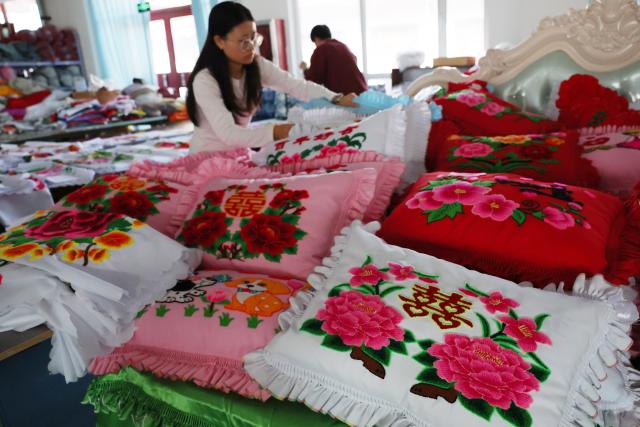 (260921) -- GUYUAN, Sept. 21, 2026 (Xinhua) -- A worker arranges Duoxiu embroidery works at a workshop in Yuanzhou District, Guyuan City of northwest China's Ningxia Hui Autonomous Region, Sept. 21, 2026. Yuanzhou District in Guyuan City has developed an integrated model combining intangible cultural heritage, original design and e-commerce, encouraging local businesses to develop original Duoxiu embroidery patterns and expand handicraft markets. The district has established 12 community handicraft workshops, creating jobs for more than 3,600 people and turning traditional skills into economic opportunities. (Xinhua/Liu Yun)