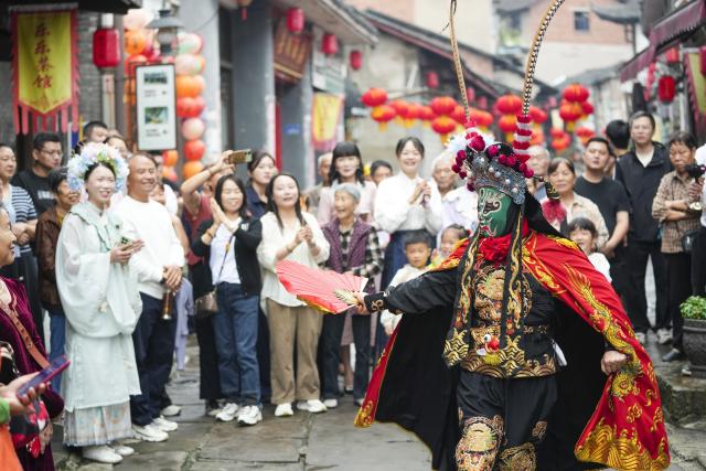 (260923) -- CHONGQING, Sept. 23, 2026 (Xinhua) -- Visitors enjoy a Sichuan Opera face-changing performance at the ancient town of Zouma in Chongqing, southwest China, Sept. 23, 2026. As the Mid-Autumn Festival and National Day holiday period approaches, the ancient town of Zouma has launched a series of folk cultural activities, including lion dance performances, an intangible cultural heritage market, a Mid-Autumn lantern riddle fair, Hanfu experiences, and Sichuan Opera face-changing performances. Integrating the historical heritage of the town's ancient post road with contemporary folk culture experiences, these activities have attracted numerous local residents and tourists. (Xinhua/Liu Chan)