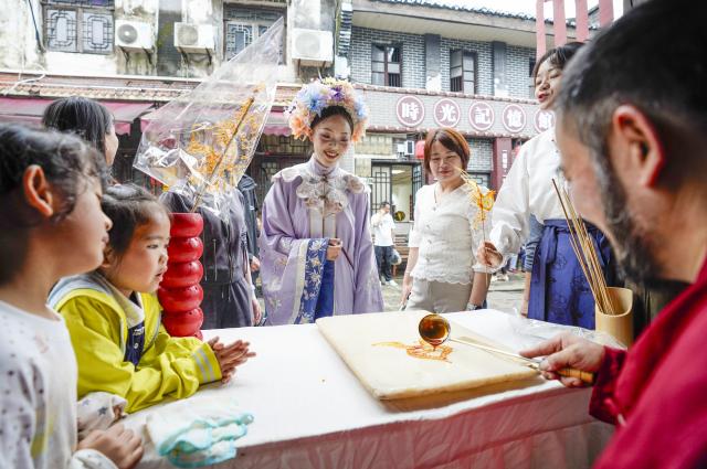 (260923) -- CHONGQING, Sept. 23, 2026 (Xinhua) -- Visitors watch a candy painting performance at the ancient town of Zouma in Chongqing, southwest China, Sept. 23, 2026. As the Mid-Autumn Festival and National Day holiday period approaches, the ancient town of Zouma has launched a series of folk cultural activities, including lion dance performances, an intangible cultural heritage market, a Mid-Autumn lantern riddle fair, Hanfu experiences, and Sichuan Opera face-changing performances. Integrating the historical heritage of the town's ancient post road with contemporary folk culture experiences, these activities have attracted numerous local residents and tourists. (Xinhua/Liu Chan)