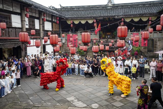 (260923) -- CHONGQING, Sept. 23, 2026 (Xinhua) -- Visitors enjoy a lion dance performance at the ancient town of Zouma in Chongqing, southwest China, Sept. 23, 2026. As the Mid-Autumn Festival and National Day holiday period approaches, the ancient town of Zouma has launched a series of folk cultural activities, including lion dance performances, an intangible cultural heritage market, a Mid-Autumn lantern riddle fair, Hanfu experiences, and Sichuan Opera face-changing performances. Integrating the historical heritage of the town's ancient post road with contemporary folk culture experiences, these activities have attracted numerous local residents and tourists. (Xinhua/Liu Chan)