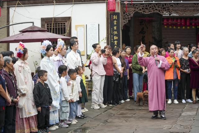(260923) -- CHONGQING, Sept. 23, 2026 (Xinhua) -- An inheritor of the national-level intangible cultural heritage "folk stories of Zouma Town" tells folk stories in the Chongqing dialect at the ancient town of Zouma in Chongqing, southwest China, Sept. 23, 2026. As the Mid-Autumn Festival and National Day holiday period approaches, the ancient town of Zouma has launched a series of folk cultural activities, including lion dance performances, an intangible cultural heritage market, a Mid-Autumn lantern riddle fair, Hanfu experiences, and Sichuan Opera face-changing performances. Integrating the historical heritage of the town's ancient post road with contemporary folk culture experiences, these activities have attracted numerous local residents and tourists. (Xinhua/Liu Chan)