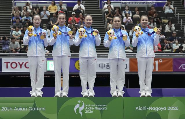 (260923) -- NAGOYA, Sept. 23, 2026 (Xinhua) -- Gold medalists Zhang Yihan, Ke Qinqin, Du Siyu, Zhang Qingying, Qiu Qiyuan (L-R) of team China pose on the podium during the awarding ceremony of the women's team final of Artistic Gymnastics at the 20th Asian Games Aichi-Nagoya 2026 in Nagoya, Japan, Sept. 23, 2026. (Xinhua/Lui Siu Wai)