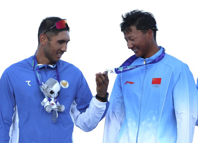 (260924) -- KAIZU, Sept. 24, 2026 (Xinhua) -- Alisher Turdiev (L) of siver medalist team Uzbekistan looks at the gold medal of Bian Shihao of team China during the awarding ceremony after the men's four final of Rowing at the 20th Asian Games Aichi-Nagoya 2026 in Kaizu of Gifu Prefecture, Japan, Sept. 24, 2026. (Xinhua/Jia Haocheng)