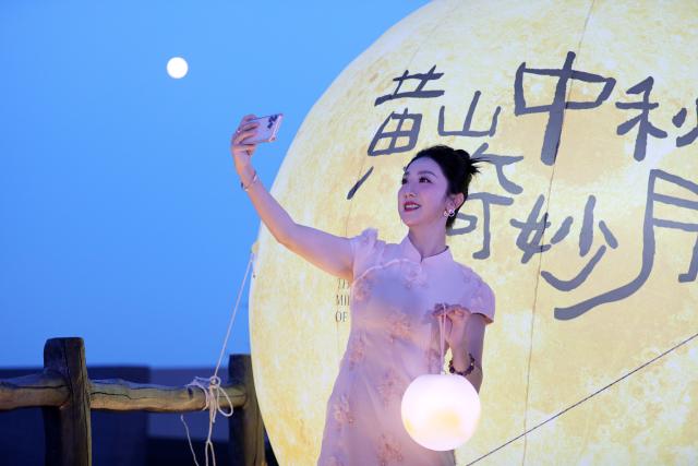 (260925) -- BEIJING, Sept. 25, 2026 (Xinhua) -- A tourist poses for selfies under the moon during a Mid-Autumn Festival activity in Huangshan Scenic Area, east China's Anhui Province, Sept. 25, 2026. The Mid-Autumn Festival falls on Sept. 25 this year. (Photo by Fan Chengzhu/Xinhua)