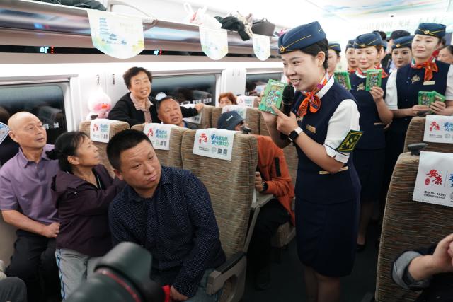 (260928) -- XI'AN, Sept. 28, 2026 (Xinhua) -- Train attendants interact with passengers on G9997, the first train of the Xi'an-Ankang high-speed railway, in northwest China's Shaanxi Province, Sept. 28, 2026. The Xi'an-Ankang high-speed railway was officially put into operation on Monday, cutting the railway travel time between Xi'an and Ankang to less than one hour. Spanning about 171 kilometers and with a design speed of 350 kilometers per hour, the railway runs through the cities of Xi'an, Shangluo and Ankang in Shaanxi Province and has five stations along the line. (Xinhua/Shao Rui)